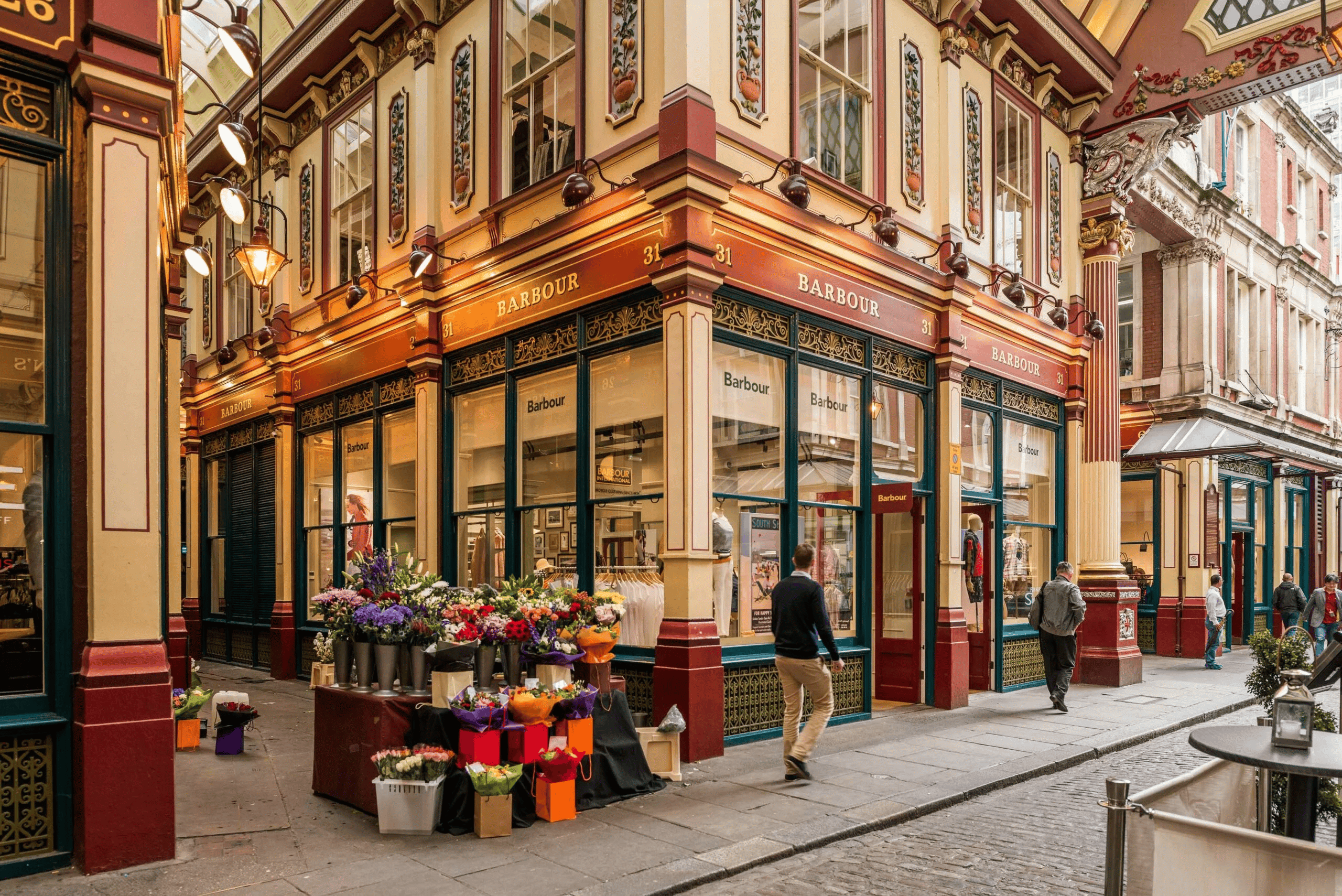 Barbour store in London's Leadenhall Market, with ornate Victorian shopfronts and a flower stall on the corner